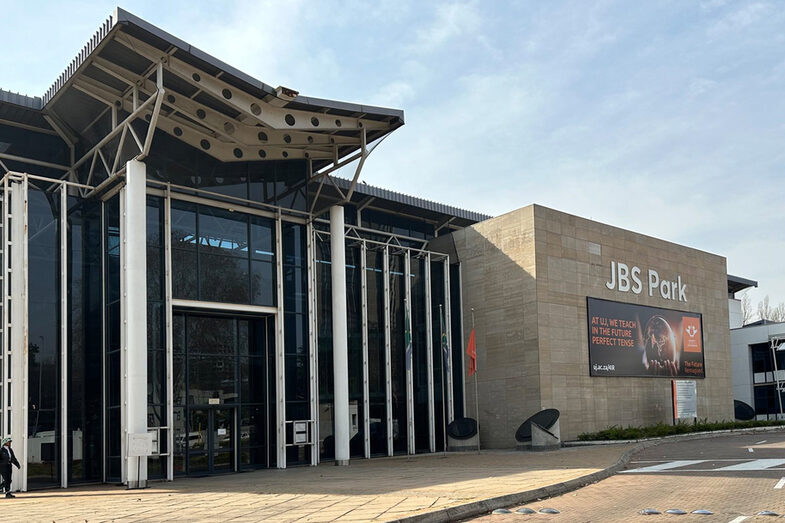 A building with a high, glazed façade, next to it a concrete extension with a large advertising poster for the University of Johannesburg.