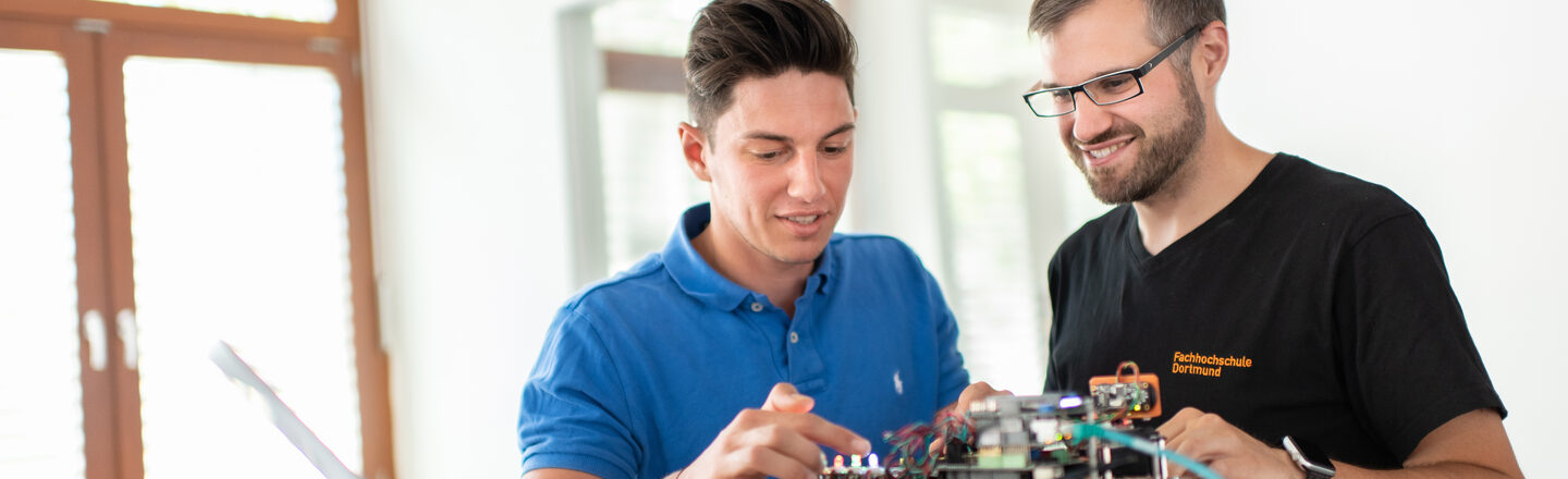 Foto eines Studenten und eines Mitarbeiters des Labors für Energieautomation und Netzführung. Sie stehen nebeneinander und arbeiten an einem elektronischen Versuchsaufbau.