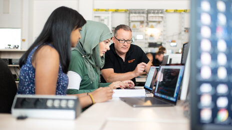 Photo of two students and a professor in the laboratory for energy automation and grid management. They are sitting next to each other and looking at a laptop screen together.