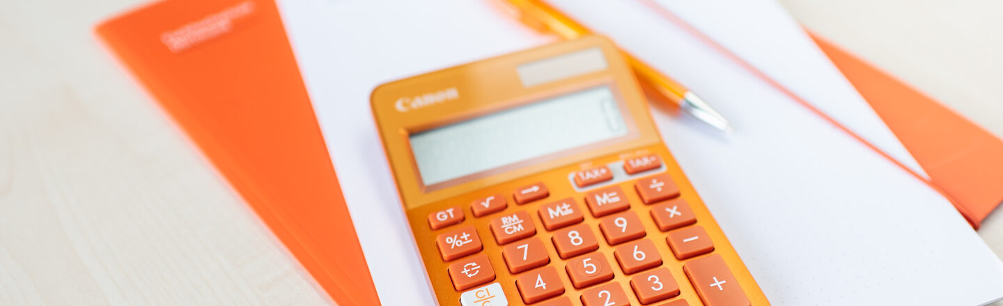 An orange calculator lies on an orange folder and a pile of notes.