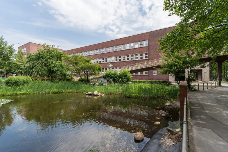 Foto mit Blick über einen Teich hin zum Gebäude des Fachbereichs Design am Max-Ophüls-Platz.