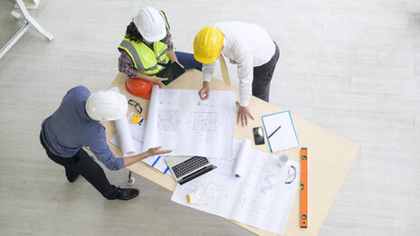 3 engineers in a meeting at a table with plans and end devices