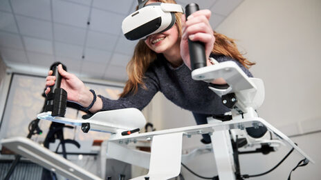 Photo of a person on the Icaros device. She is wearing VR goggles and holding on to the handles.