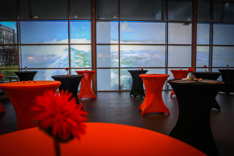 Photo of many decorated bar tables with black and orange covers standing in front of a wall onto which waves are projected.