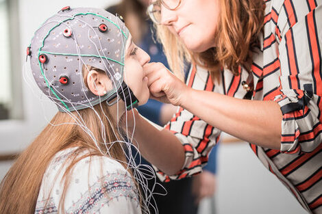 Photo of a student being fitted with an EEG mask by a woman in an orange striped blouse.