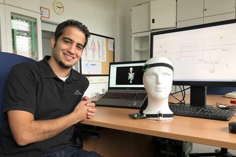 PhD student Puian Tadayon is sitting at a desk with a wired model of a head and a computer.